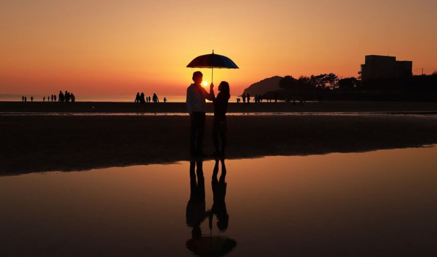 夕暮れ時の海辺で相合傘をしている男女